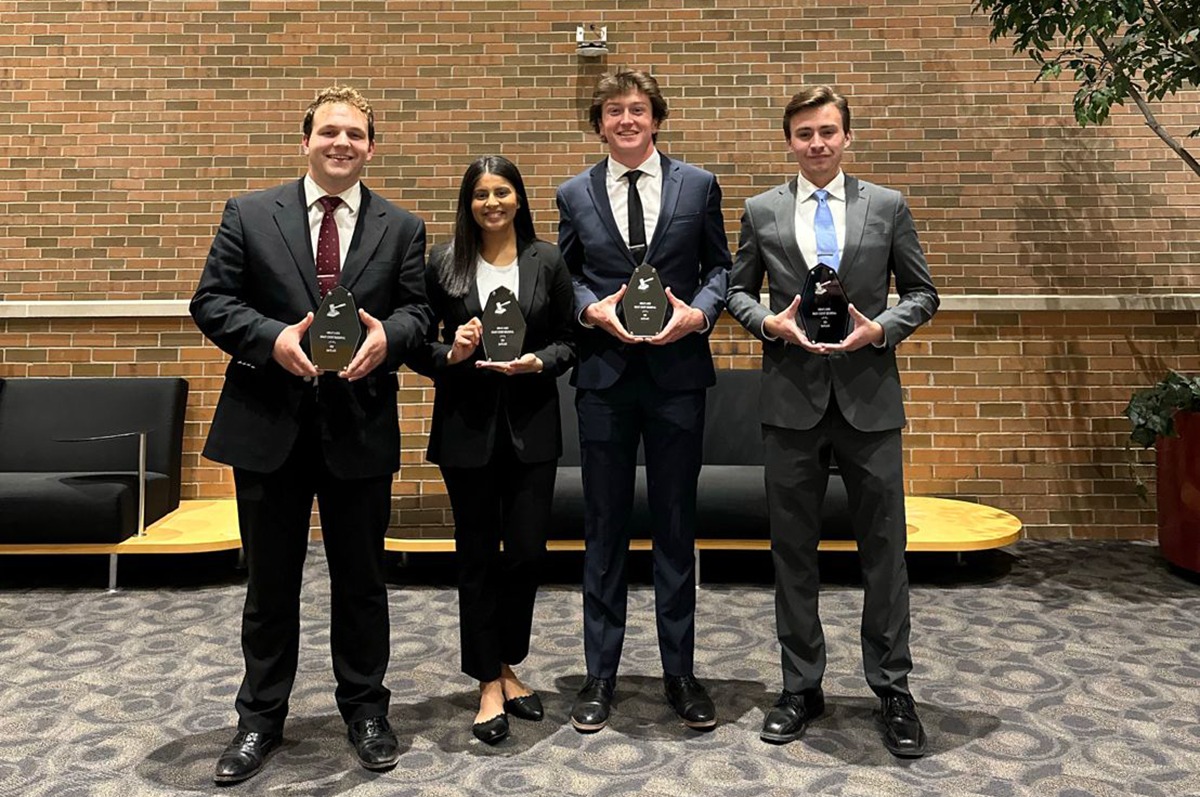 Four students in black suits holding trophies